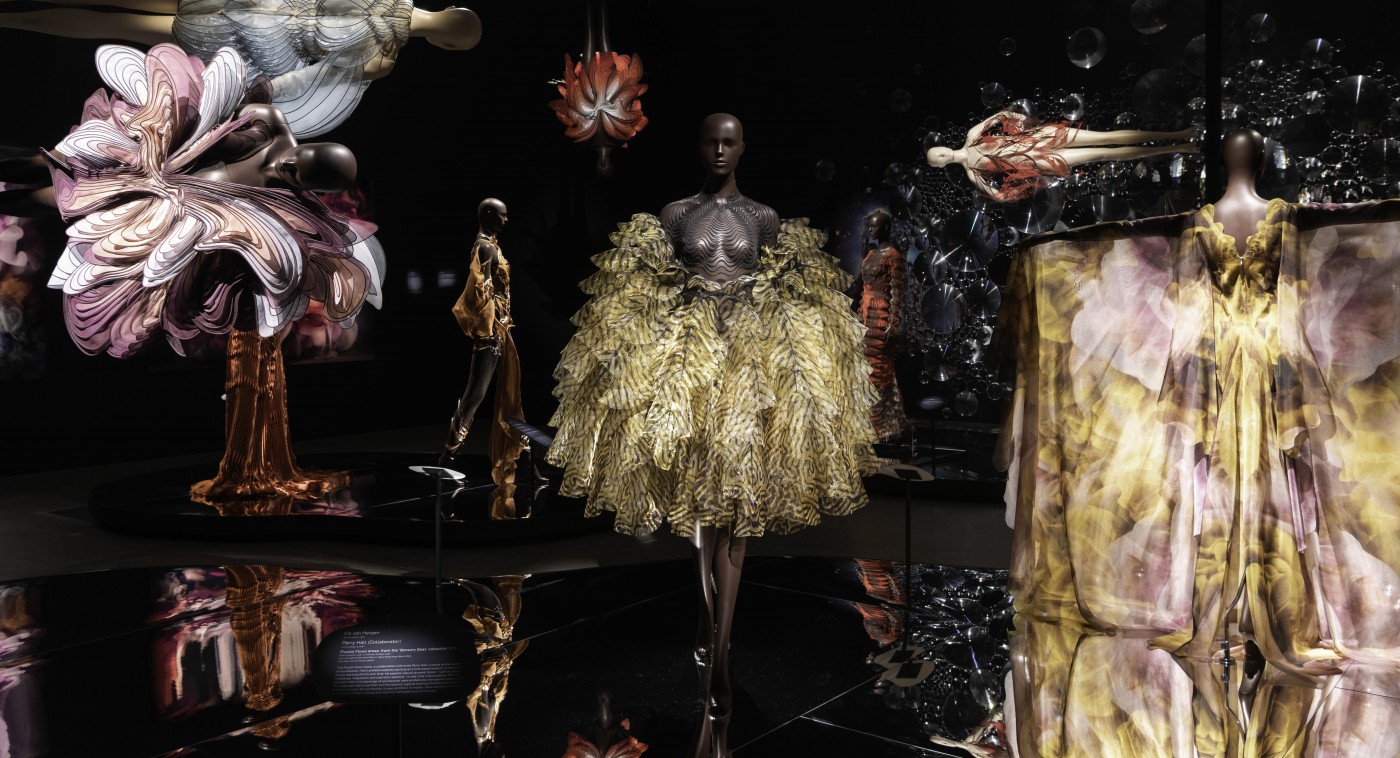 Installation view of ‘Iris van Herpen: Sculpting the Senses’ including (front l-r) Symbiotic asymmetric dress, from the ‘Shift Souls’ collection 2019 by Iris van Herpen; Fractal Flows dress, from the ‘Sensory Seas’ collection 2020 by Iris van Herpen with collaborator Perry Hall; and Cosmica gown, from the ‘Shift Souls’ collection 2019 by Iris van Herpen with collaborator Kim Keever / © Iris van Herpen / Photograph: C Callistemon © QAGOMA