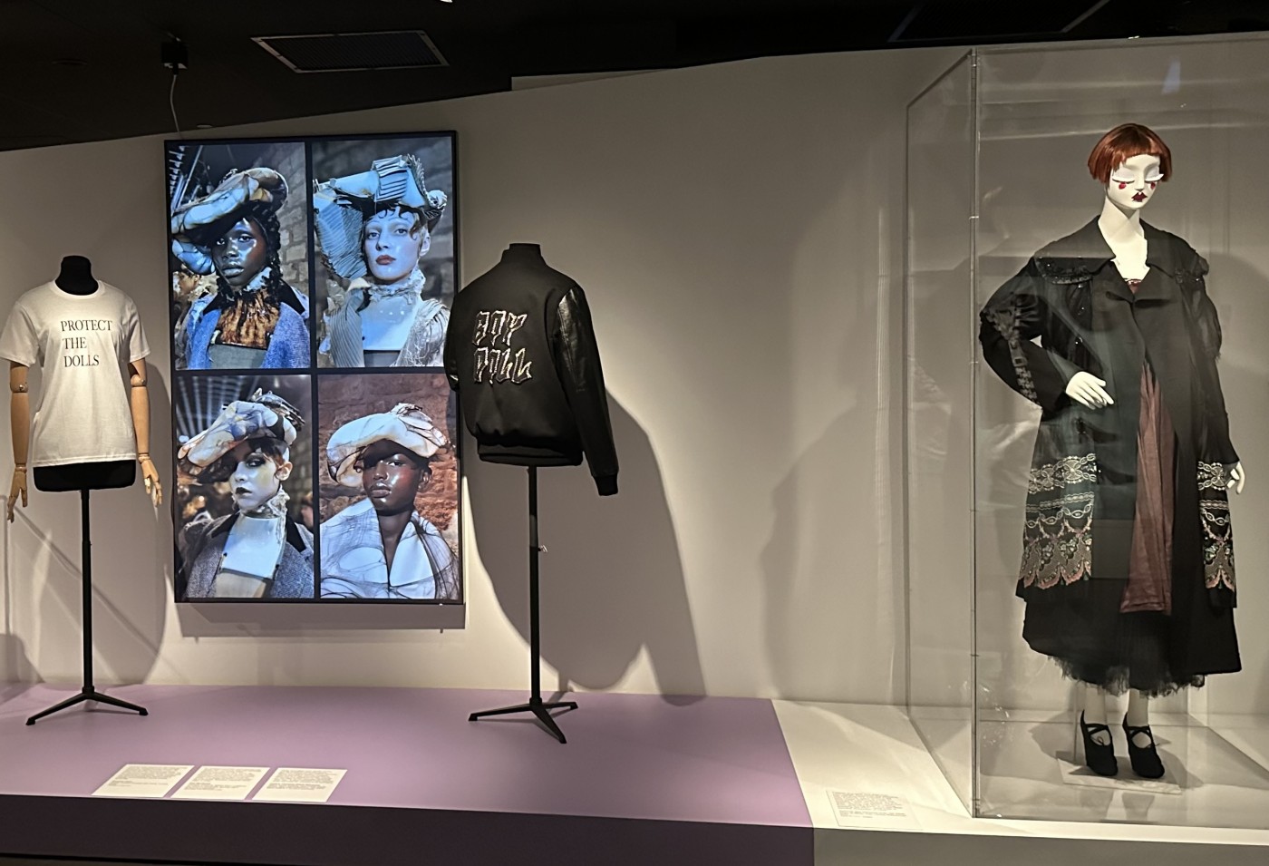 “We Can All Be Dolls” with framed artwork by Courtney Charles and photographs from Pat McGrath for Maison Margiela (on lightbox). In small case: Barbie wearing a “Black Dolls Matter” T-shirt by Mark Ruffin and a Laverne Cox Barbie. On dress forms: “Protect the Dolls” T-shirt by Conner Ives (left) and “Boy Doll” jacket by Celine Homme (right). In large case: an ensemble on loan from Lynn Yaeger. © Image Jane Francis