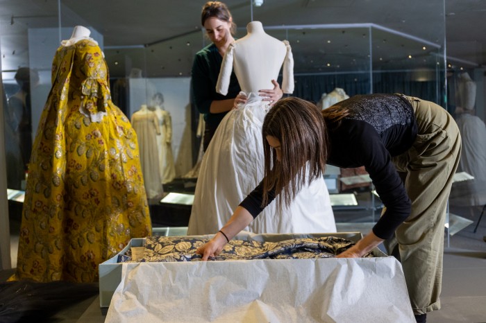 Textile Conservator Sarah Glenn and Collection Manager Elly Summers packing away a 1750s blue and cream woven silk gown in the Fashion Museum galleries