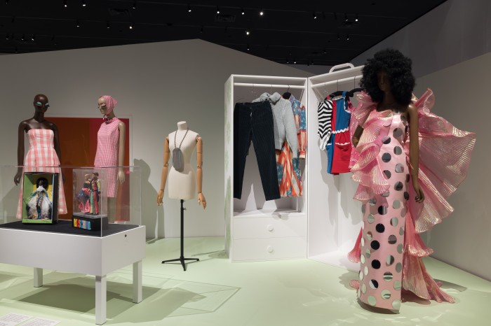 Partial views of the “Pink Gingham” and “Barbie” sections. Far left: dress by Zara x Barbie: The Movie, reproduction Biba dress and headscarf by Matthew Carlsen. In case: “Mbili” Barbie by Byron Lars (left) and Moschino Barbie and Ken dolls. Center, on dress form: enlarged G.I. Joe dog tag by Maison Martin Margiela. Fashion case featuring Barbie-inspired designs from left to right: trousers by Maison Martin Margiela, sweater by Maison Martin Margiela, dress by Catherine Malandrino, swimsuit by Barbie x Unique Vintage, dress by Fashion Brand Company, and dress by Jeremy Scott. On mannequin: dress by Jeremy Scott for Moschino. © Museum at FIT