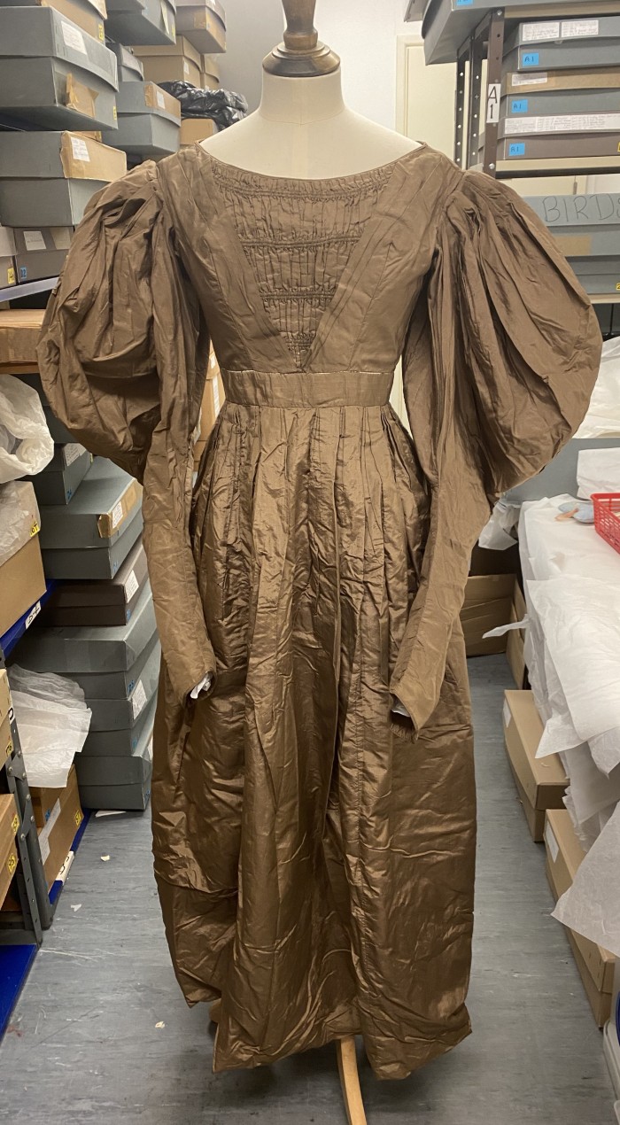Brown silk Victorian dress with leg-of-mutton sleeves, boat neck, and full pleated skirt.