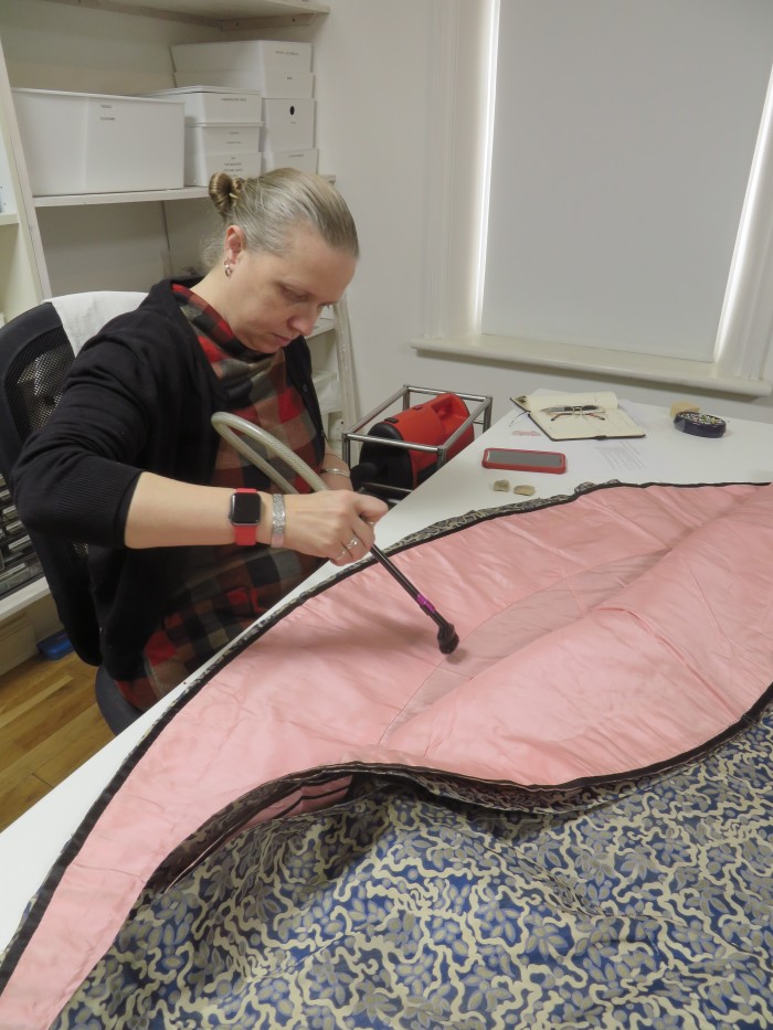 Senior conservator Elizabeth Cherry suction cleaning the blue and cream ensemble worn by Marion to her daughter Maud’s wedding.